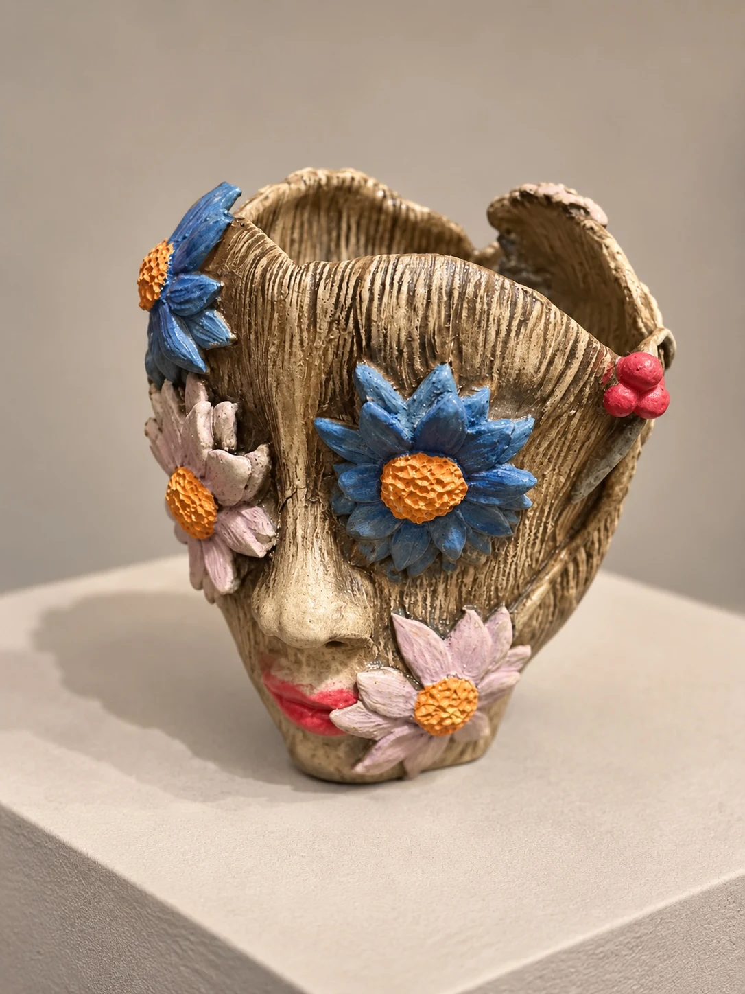 Sculptural face vessel with bark-like texture and raised blue and pink flowers